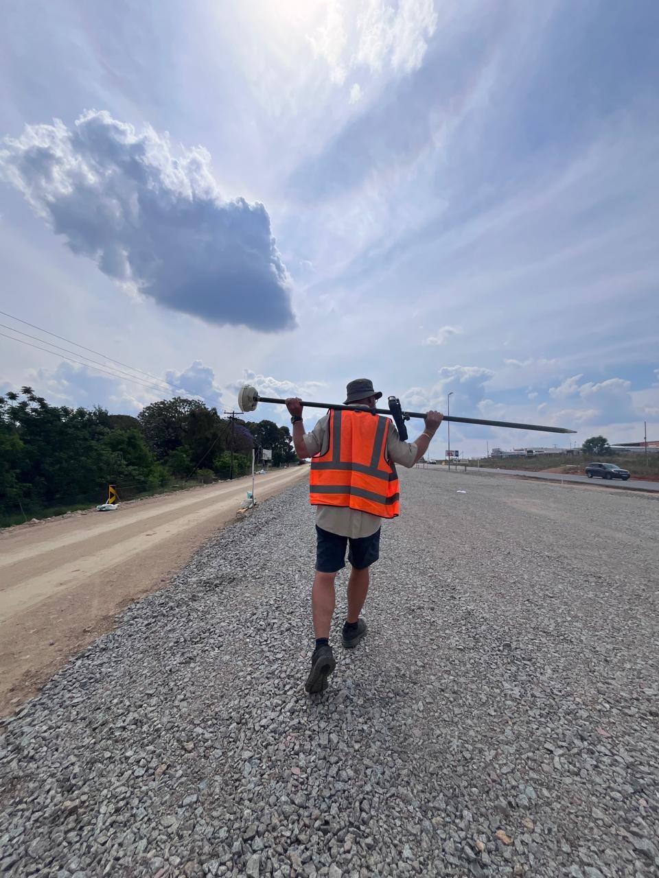 Surveyor carrying GNSS equipment along an active roadworks site