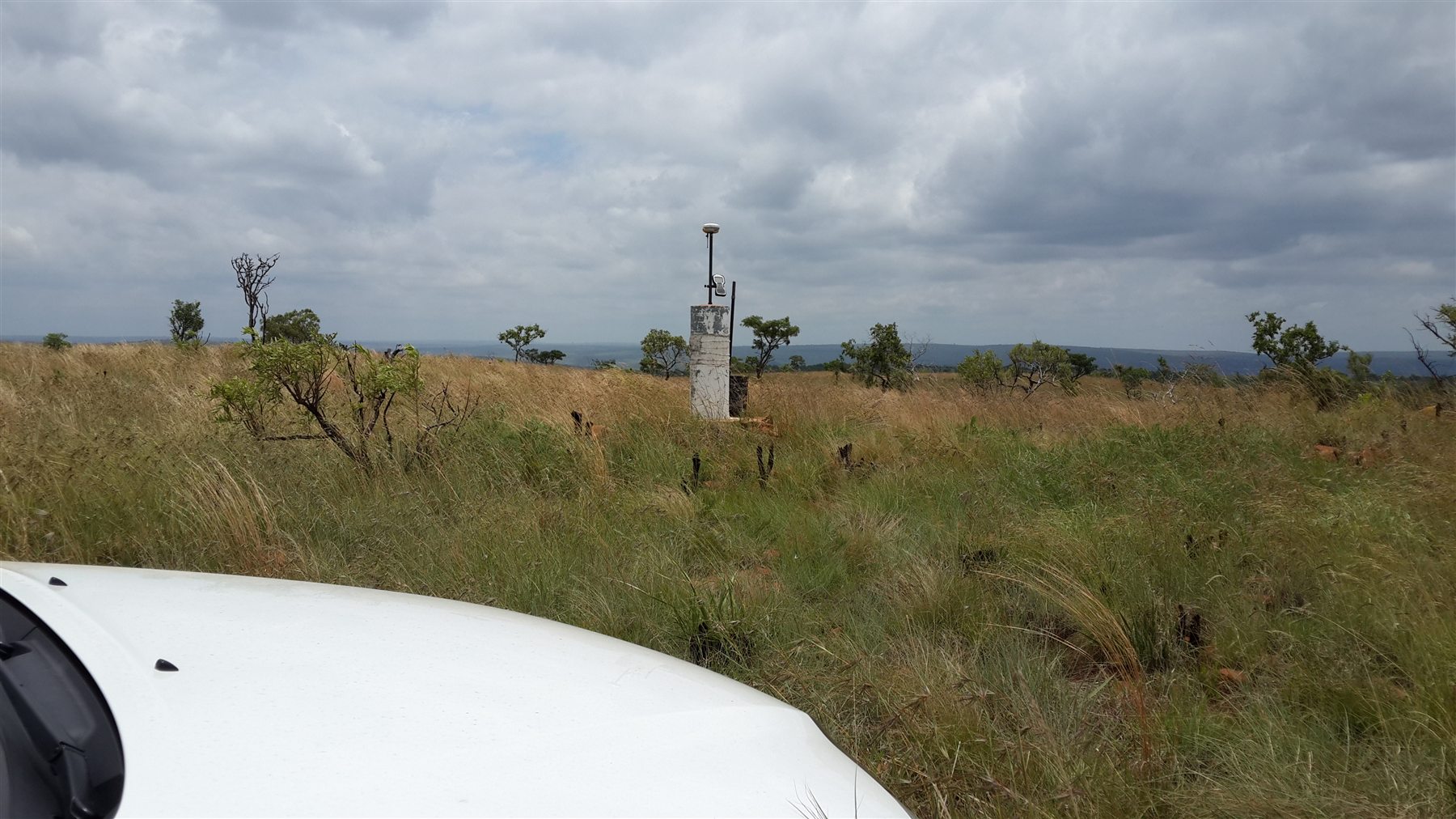 Established survey control pillar in open elevated terrain beneath an overcast sky